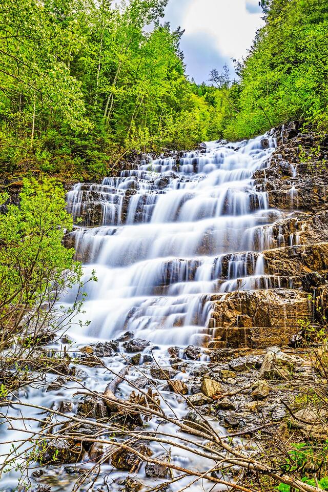 Silver Staircase Falls gracefully cascades 40 feet down the cliffs in Glacier National Park, painting the tiered cliffs in silver paint made of water.