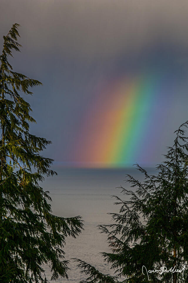 A rainbow shines through a parting storm across the mouth of the Columbia River in Astoria, Oregon on the Oregon Coast.