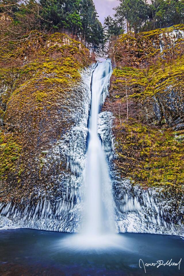 Ice clings to the cliffs in the Columbia River Gorge during a cold spell, as Horsetail Falls gracefully tumbles over the cliffs and down into the pool of water.