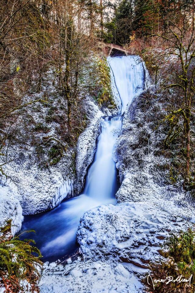 Winter snow and ice cling to the basalt cliffs in the Columbia River Gorge during a cold spell, as Bridal Veil Falls gracefully tumbles 118 feet over the cliffs