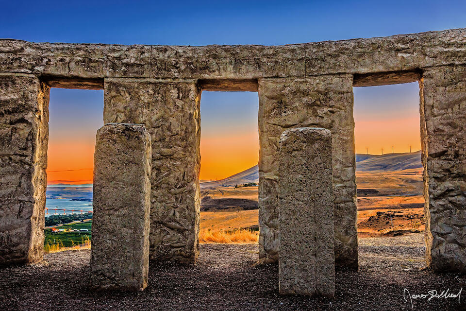 Sunset bathes the sky, as a warm glow shines between the pillars reflecting a soft glow onto the stone and the hills of the Columbia River Gorge.