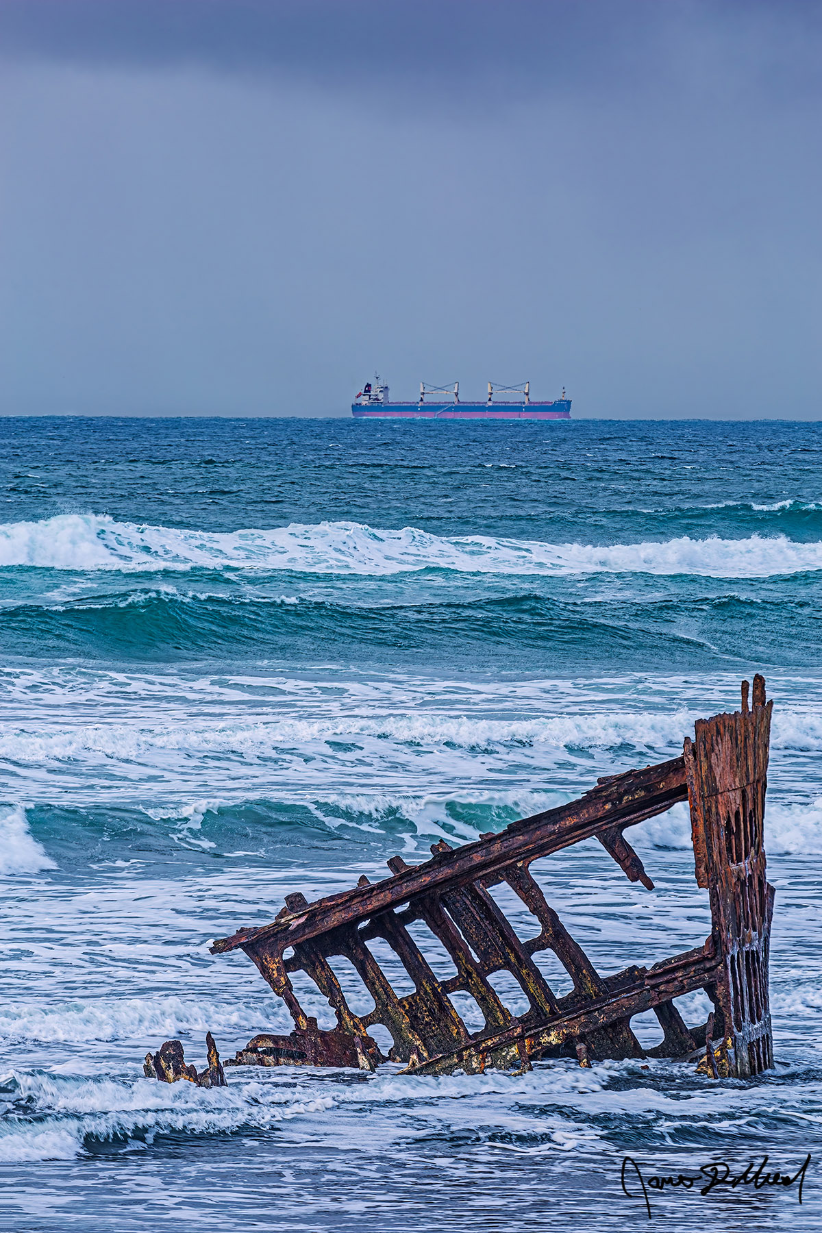 Temporal Alignment Waves during King Tides pound the Wreck of the Peter Iredale on the North Oregon Coast near Astoria as a large ocean going cargo vessel passes far behind it.