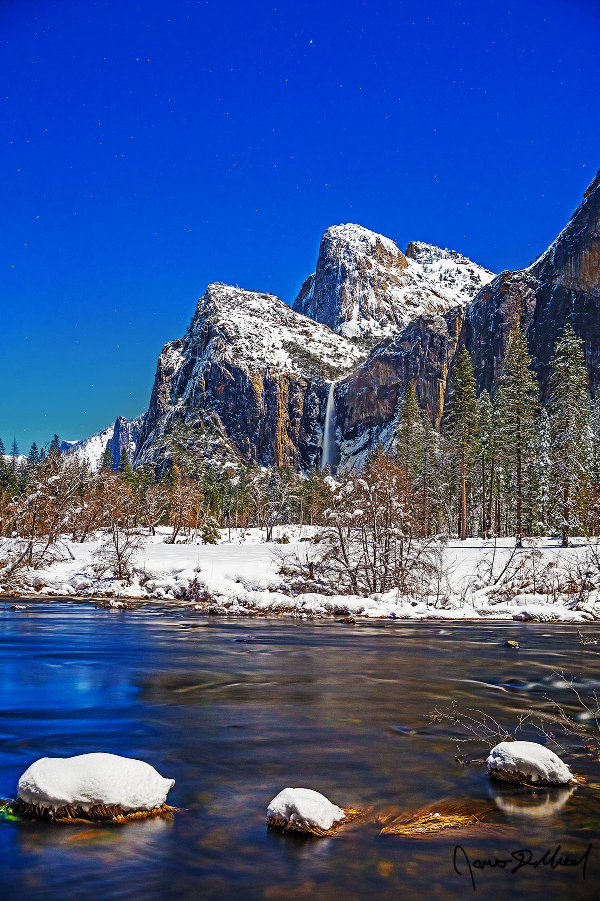 Winter's Bride Moonlight illuminates Yosemite Valley Cathedral Rocks, Bridalveil Fall and the Merced River in the winter as snow blankets the ground on a cold winter night.