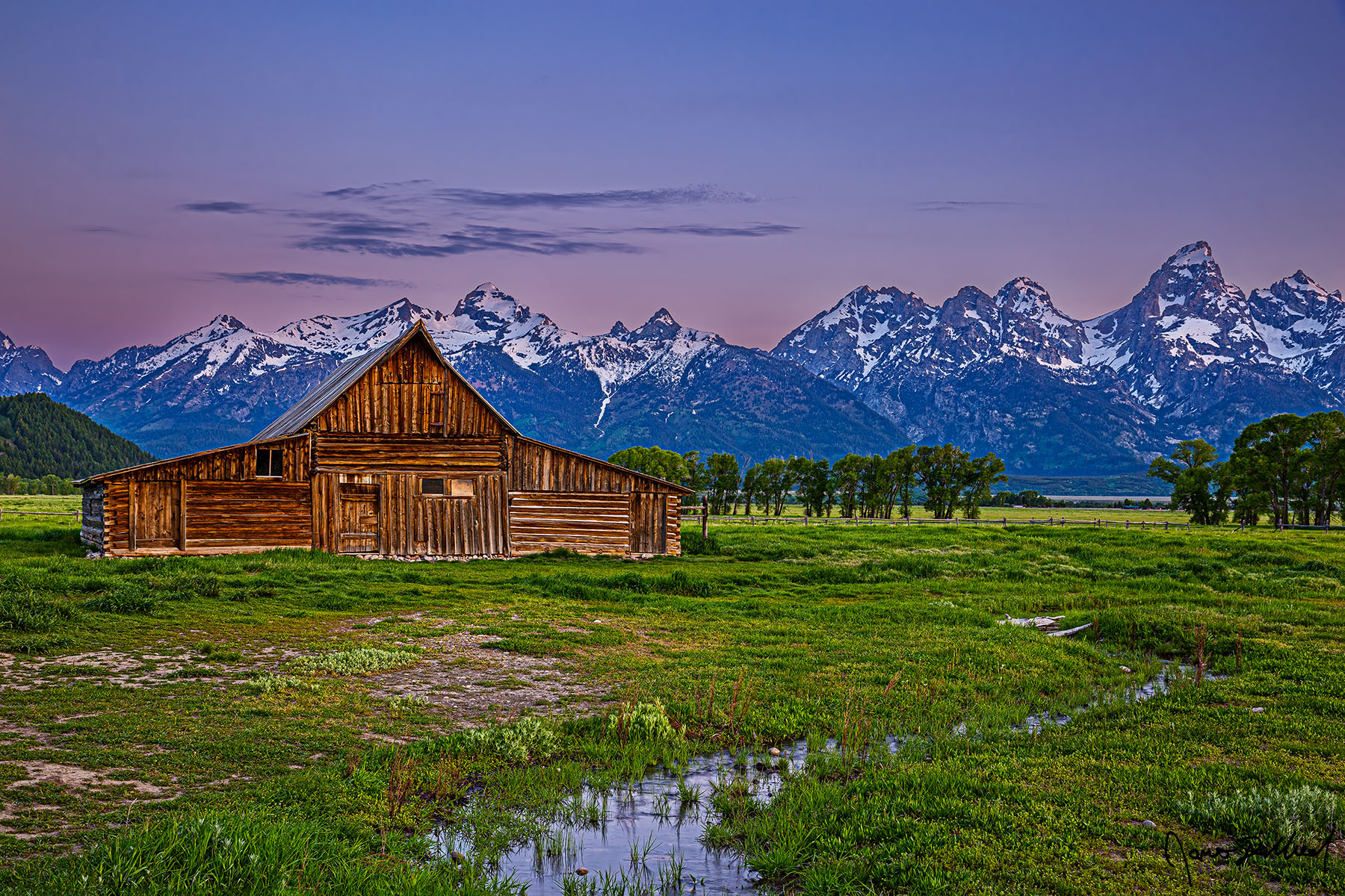 Revived - Sunrise over the TA Moulton Barn and the Teton Range in Grand Teton National Park Alpenglow before sunrise illuminates the tops of the Teton Range as a small creek runs through a meadow in front of the TA Moulton Barn.