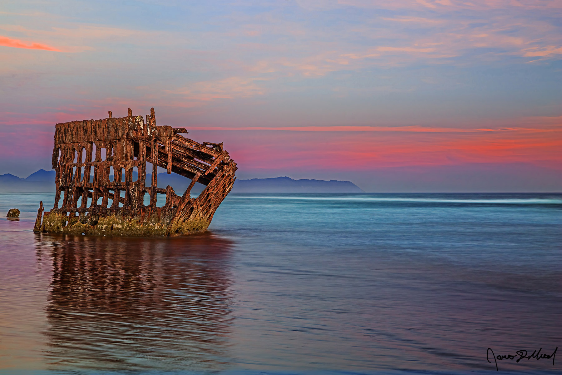 Wrecked Sunset The waters of the Pacific Ocean flow up around the Wreck of the Peter Iredale at sunset, as the shipwreck faintly reflects in the waters of the incoming tide.