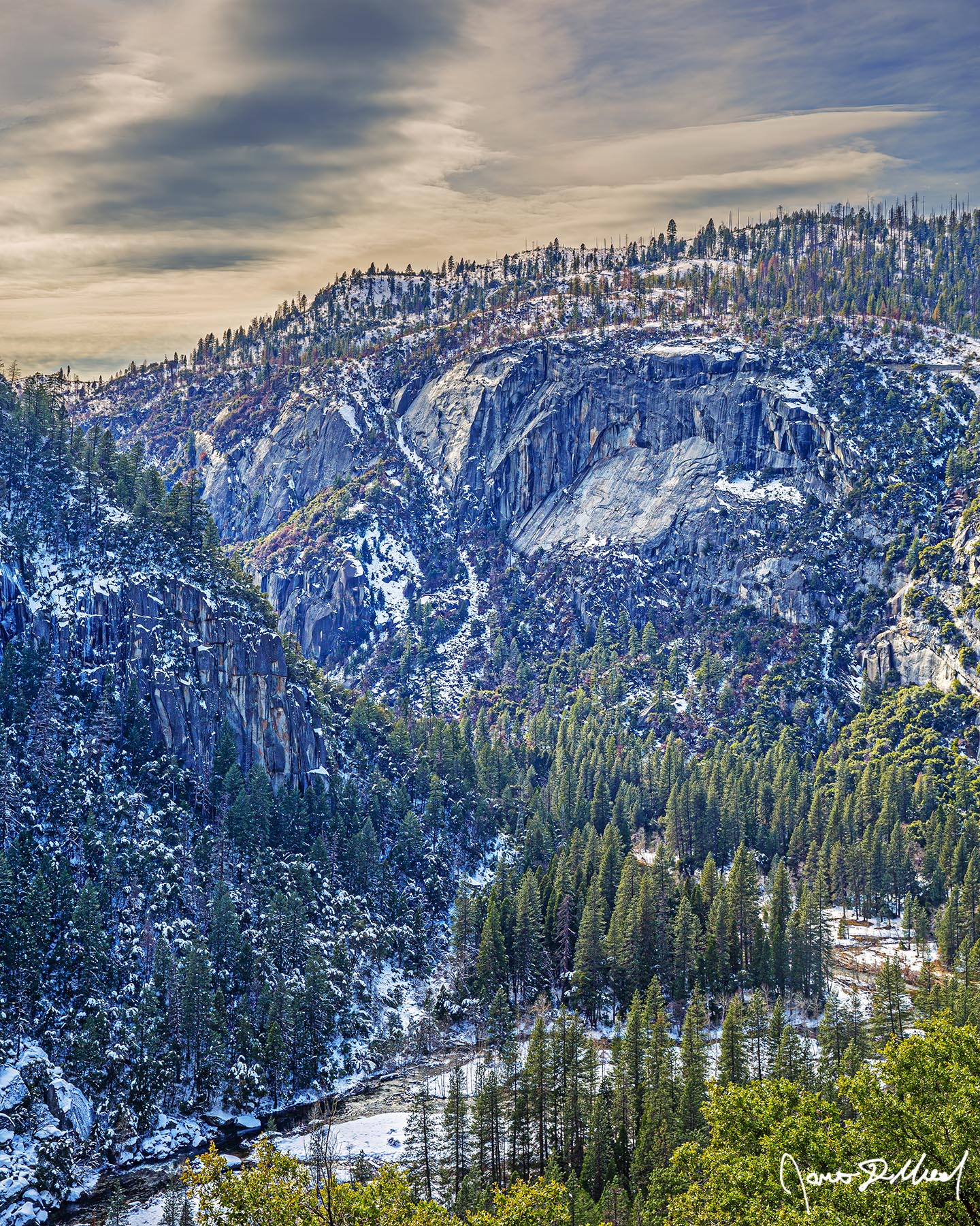 A Cut Above The Merced River cuts through snow covered Merced River Canyon in Yosemite National Park as sunlight illuminates the clouds and the snow on the cliffs above