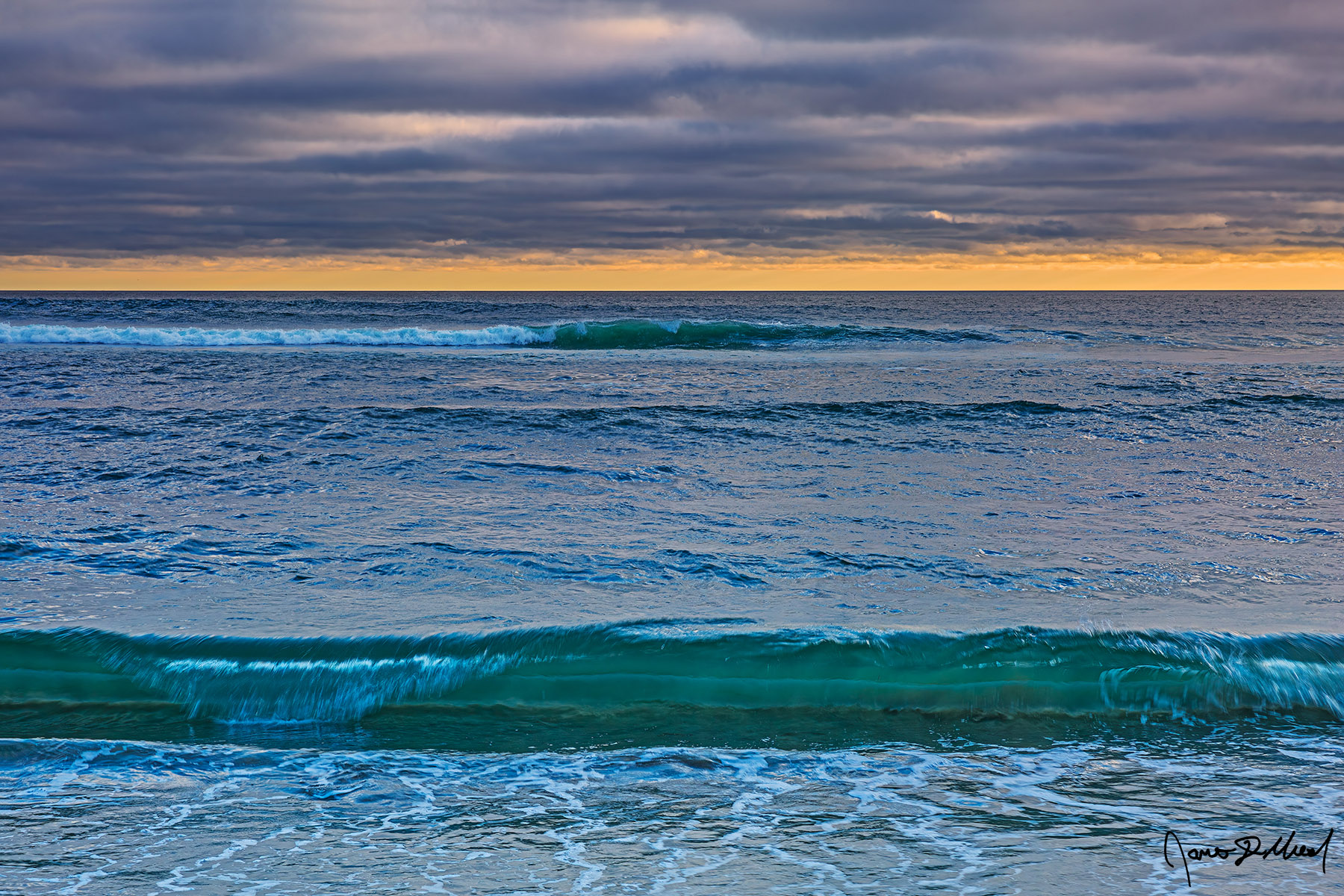 Rolling with the Tide Emerald Waves in the Pacific Ocean roll towards the shore at sunset as warm colors show through the cloud breaks and along the horizon.