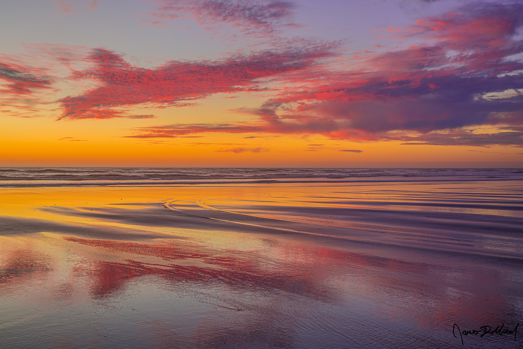 Road to Nowhere An array of color at sunset over the Pacific Ocean reflects in the sand. A lone set of tire tracks leads out towards the tide line as if a road to nowhere